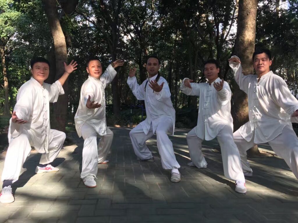 五位練習者穿著白色太極服,在樹林中擺出太極招式