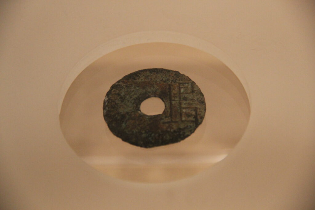 一枚古代中國圓形方孔銅錢置於透明展示座特寫,呈現易經占卜的文化意象