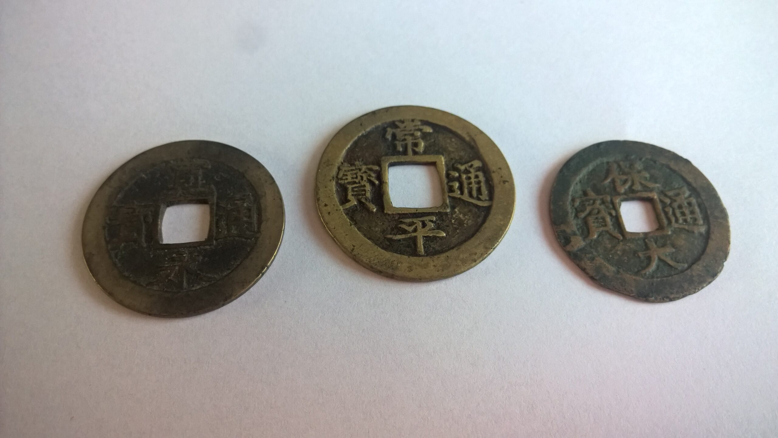 三枚大小不一的古代中國方孔銅錢並排放置，象徵易經占卜擲錢問卦的傳統工具